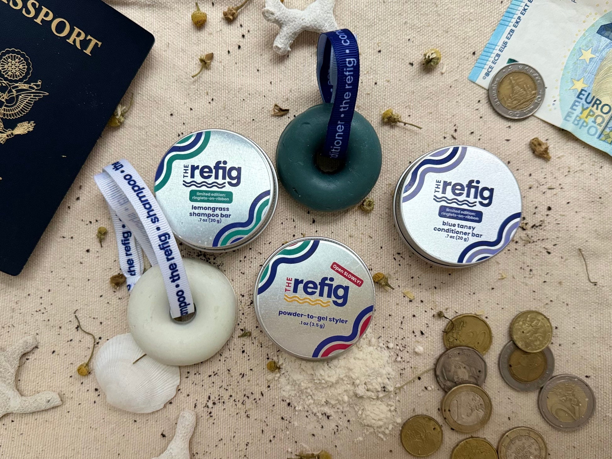 Wash-and-Go travel hair care kit. Shampoo bar tin, conditioner bar tin and powder-to-gel styler tin next to international coins and passport. Juxtaposition of elements to demonstrate size and connection to travel.